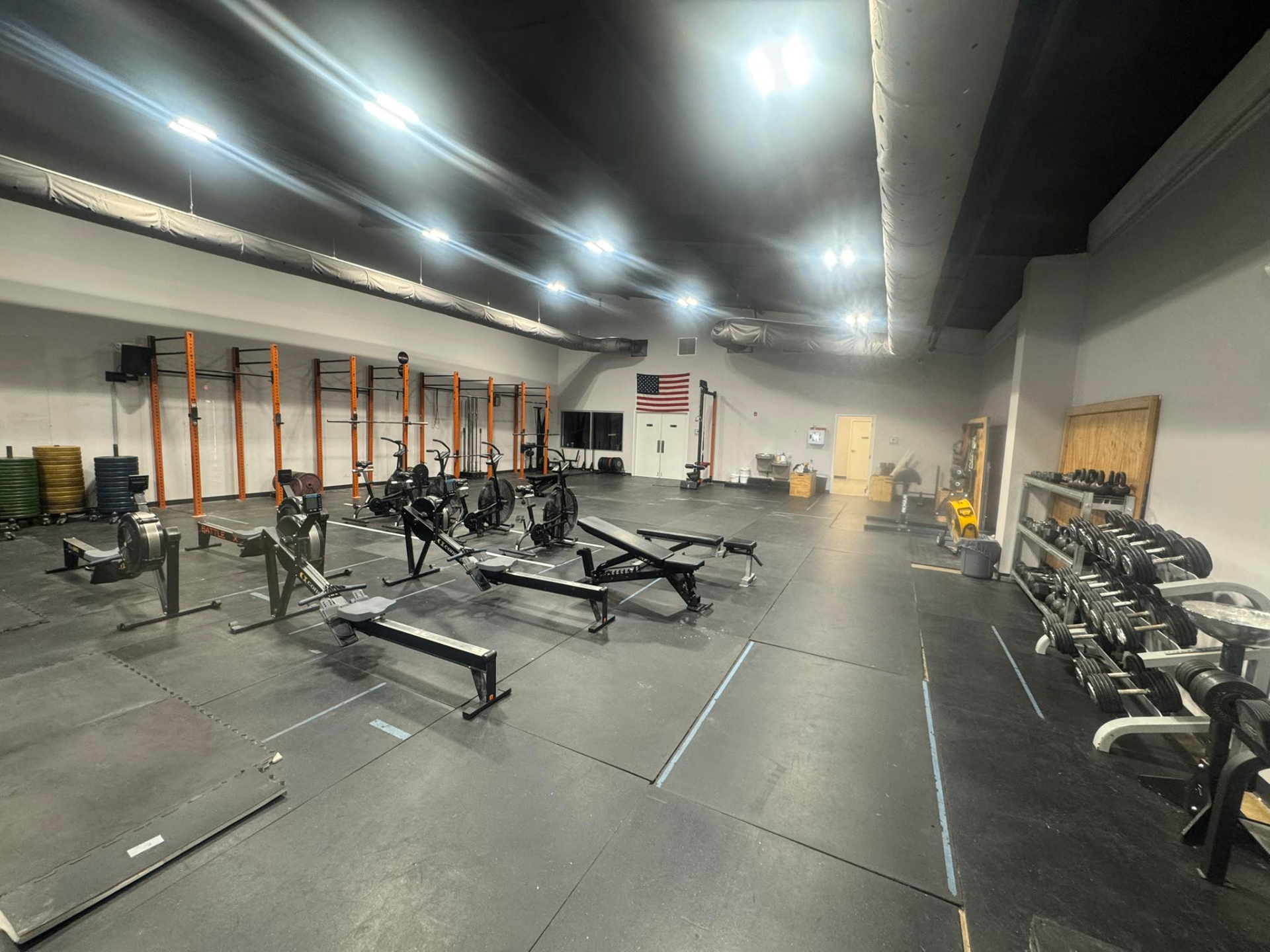 Wide view of the open gym floor with Concept2 rowers, air bikes, squat racks, and dumbbells